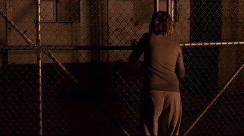 Movie still from “Blindness” (2008), directed by Fernando Meirelles – A woman standing in front of a chain link fence at night; Wide shot, Over the shoulder angle