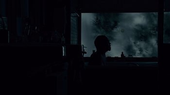 Movie still from “Blindness” (2008), directed by Fernando Meirelles – A man sitting in front of a television in a dark room; Medium shot, Low angle