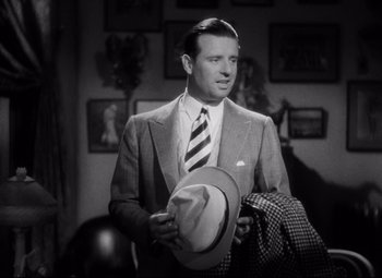 Movie still from “Blonde Venus” (1932), directed by Josef von Sternberg – A man in a suit and tie holding a hat; Medium shot, High angle