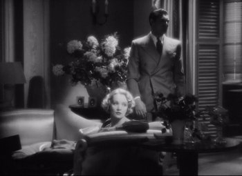 Movie still from “Blonde Venus” (1932), directed by Josef von Sternberg – A man and a woman standing in front of a table with flowers on top of it; Medium shot, High angle