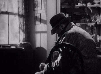 Movie still from “Blonde Venus” (1932), directed by Josef von Sternberg – An old man sitting in a chair looking down at a book; Medium shot, High angle