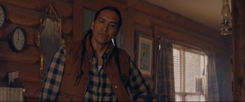 Movie still from “Blood Quantum” (2019), directed by Jeff Barnaby – A man in a plaid shirt is standing in a living room; Medium shot, Over the shoulder angle