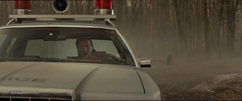 Movie still from “Blood Quantum” (2019), directed by Jeff Barnaby – A man sitting in the drivers seat of a police car; Medium shot, Over the shoulder angle
