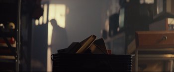 Movie still from “Blood Quantum” (2019), directed by Jeff Barnaby – A pile of books sitting on top of a table; Medium shot, Over the shoulder angle