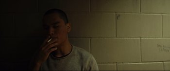 Movie still from “Blood Quantum” (2019), directed by Jeff Barnaby – A young man smoking a cigarette in a room; Close Up shot, Low angle