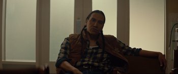 Movie still from “Blood Quantum” (2019), directed by Jeff Barnaby – A man sitting in a chair wearing a plaid shirt; Medium shot, Over the shoulder angle