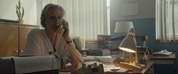 Movie still from “Blood Quantum” (2019), directed by Jeff Barnaby – An older woman sitting at a desk talking on the phone; Medium shot, Low angle