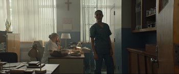 Movie still from “Blood Quantum” (2019), directed by Jeff Barnaby – A woman standing in front of a desk in a room; Wide shot, Low angle