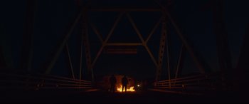 Movie still from “Blood Quantum” (2019), directed by Jeff Barnaby – Two people standing in front of a fire at night under a bridge; Extreme Wide shot, Low angle
