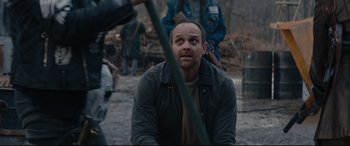 Movie still from “Blood Quantum” (2019), directed by Jeff Barnaby – A man sitting on the ground in front of other people; Medium shot, Over the shoulder angle