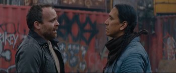 Movie still from “Blood Quantum” (2019), directed by Jeff Barnaby – Two men standing next to each other in front of a wall; Medium shot, Over the shoulder angle