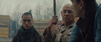 An older man holding a sword in front of two other men