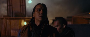 A man with long black hair wearing a brown jacket