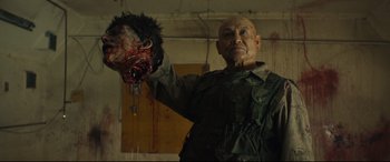 Movie still from “Blood Quantum” (2019), directed by Jeff Barnaby – A man holding a bloody head in a room; Close Up shot, Over the shoulder angle