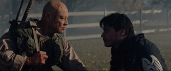 Movie still from “Blood Quantum” (2019), directed by Jeff Barnaby – A man and a man in a field with trees in the background; Medium shot, Over the shoulder angle
