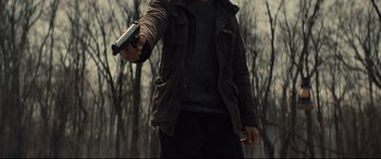 Movie still from “Blood Quantum” (2019), directed by Jeff Barnaby – A man holding a gun while standing in the woods; Medium shot, Over the shoulder angle