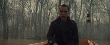 Movie still from “Blood Quantum” (2019), directed by Jeff Barnaby – A man sitting on top of a wooden bench in front of trees; Medium shot, Low angle