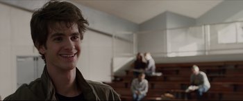 Movie still from “The Amazing Spider-Man” (2012), directed by Marc Webb – A young man smiling in front of a group of people; Close Up shot, Over the shoulder angle