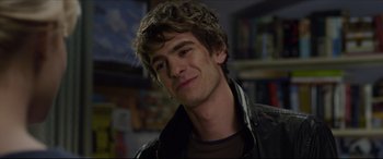 Movie still from “The Amazing Spider-Man” (2012), directed by Marc Webb – A young man with curly brown hair smiles for the camera; Close Up shot, Over the shoulder angle