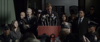 Movie still from “The Amazing Spider-Man” (2012), directed by Marc Webb – A man is speaking at a press conference; Medium shot, Over the shoulder angle