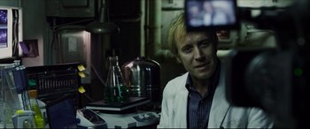 Movie still from “The Amazing Spider-Man” (2012), directed by Marc Webb – A man in a lab coat sitting in front of a camera; Close Up shot, Over the shoulder angle