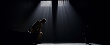 A man kneeling down in front of a jail cell