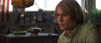Movie still from “Blow” (2001), directed by Ted Demme – A man with long blonde hair sitting at a table; Close Up shot, High angle