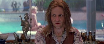 Movie still from “Blow” (2001), directed by Ted Demme – A man with long brown hair and wearing a floral shirt; Close Up shot, Over the shoulder angle