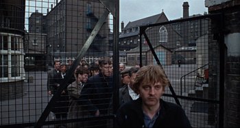 Movie still from “Blow-Up” (1966), directed by Michelangelo Antonioni – A group of people standing in front of a fence; Wide shot, High angle