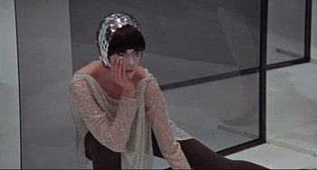 Movie still from “Blow-Up” (1966), directed by Michelangelo Antonioni – A woman sitting on the ground wearing a silver hat; Medium shot, Low angle