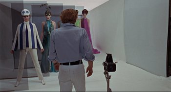 Movie still from “Blow-Up” (1966), directed by Michelangelo Antonioni – A group of people in a room with a camera; Wide shot, Over the shoulder angle