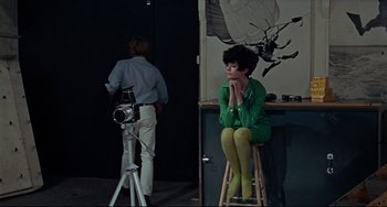 Movie still from “Blow-Up” (1966), directed by Michelangelo Antonioni – A woman sitting on top of a stool in front of a camera; Wide shot, High angle