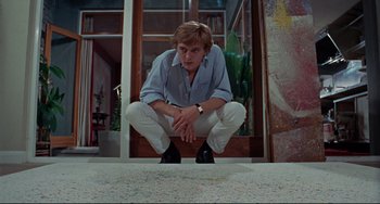 Movie still from “Blow-Up” (1966), directed by Michelangelo Antonioni – A man crouching on the ground in front of a building; Wide shot, Low angle