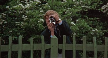 Movie still from “Blow-Up” (1966), directed by Michelangelo Antonioni – A man taking a picture of himself through a fence; Medium shot, Low angle