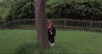 Movie still from “Blow-Up” (1966), directed by Michelangelo Antonioni – A man taking a picture of a tree with a camera; Medium shot, Low angle