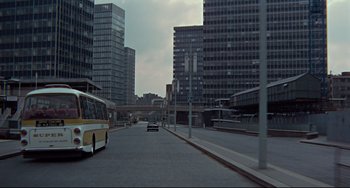 Movie still from “Blow-Up” (1966), directed by Michelangelo Antonioni – A bus driving down a street next to tall buildings; Extreme Wide shot, High angle