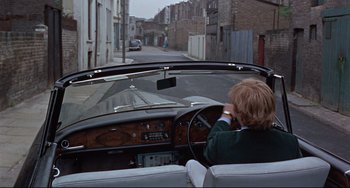 Movie still from “Blow-Up” (1966), directed by Michelangelo Antonioni – A woman driving a car down a street; Wide shot, High angle