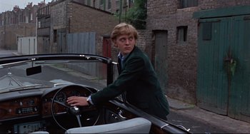 Movie still from “Blow-Up” (1966), directed by Michelangelo Antonioni – A man in a suit sitting in the driver's seat of a car; Medium shot, Over the shoulder angle