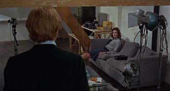 Movie still from “Blow-Up” (1966), directed by Michelangelo Antonioni – A woman sitting on top of a couch in a living room; Wide shot, Over the shoulder angle