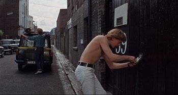 Movie still from “Blow-Up” (1966), directed by Michelangelo Antonioni – A shirtless young man leaning against a building; Wide shot, Over the shoulder angle