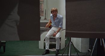 Movie still from “Blow-Up” (1966), directed by Michelangelo Antonioni – A man sitting on a chair in front of a camera; Medium shot, High angle