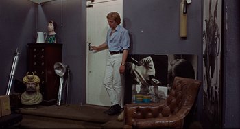 Movie still from “Blow-Up” (1966), directed by Michelangelo Antonioni – A man standing in front of a wall holding a remote control; Wide shot, Over the shoulder angle