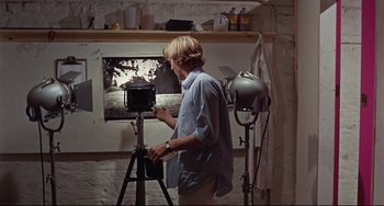 Movie still from “Blow-Up” (1966), directed by Michelangelo Antonioni – A man standing in front of a camera in a room; Medium shot, High angle
