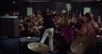 Movie still from “Blow-Up” (1966), directed by Michelangelo Antonioni – A group of people watching a man on a stage; Wide shot, High angle