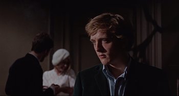 Movie still from “Blow-Up” (1966), directed by Michelangelo Antonioni – A man in a suit and tie in front of two other people; Close Up shot, Over the shoulder angle