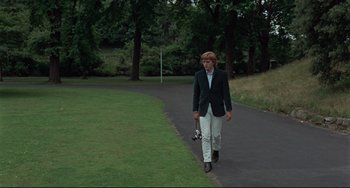 Movie still from “Blow-Up” (1966), directed by Michelangelo Antonioni – A young man walking down a path holding a camera; Wide shot, Low angle