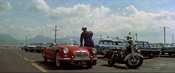 Movie still from “Blue Hawaii” (1961), directed by Norman Taurog – A man standing in the back of a red car; Extreme Wide shot, Low angle