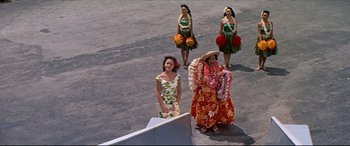 Movie still from “Blue Hawaii” (1961), directed by Norman Taurog – A group of hula dancers standing next to each other on the street; Wide shot, High angle