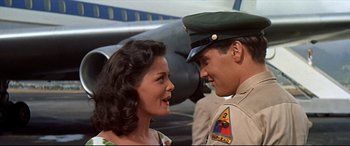 Movie still from “Blue Hawaii” (1961), directed by Norman Taurog – A man and a woman smiling at each other in front of an airplane; Medium shot, Over the shoulder angle