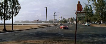 Movie still from “Blue Hawaii” (1961), directed by Norman Taurog – A red car driving down a street next to a body of water; Extreme Wide shot, High angle